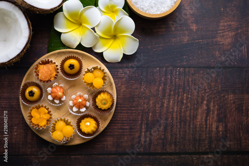Traditional golden Thai sweets are placed on a wooden table, adorned with banana leaves and flowers