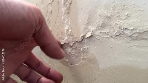Close up hand peeling damaged wall paint and flaking plaster