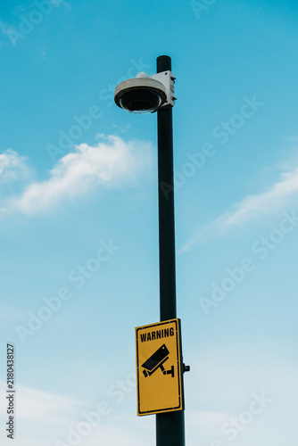 Foto A surveillance camera and warning sign stand on a pole against a blue sky