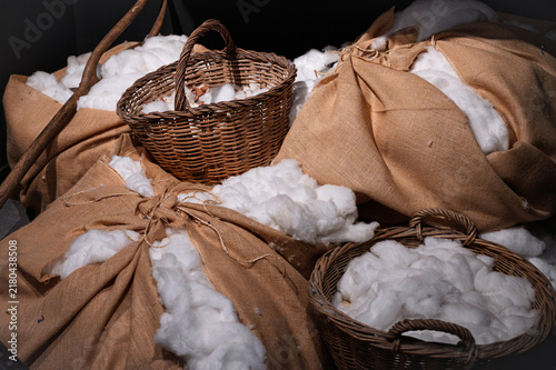 Raw white cotton in burlap sacks and woven wicker baskets stored inside a historical ship cargo hold.