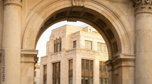 Art deco style building viewed through stone archway with carved columns. Historic architecture facade with ornamental details and large windows at