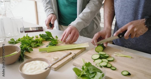 Right person is starting by slicing cucumber while left person is chopping celery for salad prep