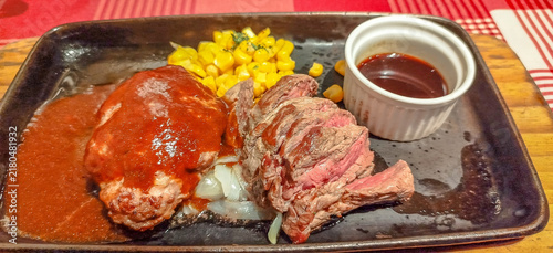 Foto A sizzling Japanese-style combination plate featuring a juicy beef steak and a savory hambagu patty served on a hot black iron pan with sweet corn and rich gravy sauce