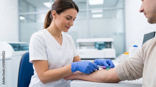 Female phlebotomist drawing a blood sample from a male patient's arm in a diagnostic lab