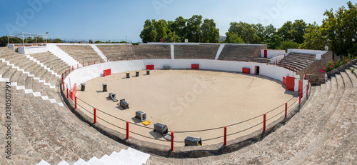 Interior of the plaza de toros bullring in Alcúdia, on the island of Mallorca, Balearic Islands, Spain, showing the sand-covered arena floor and tiered concrete seating with red railings.