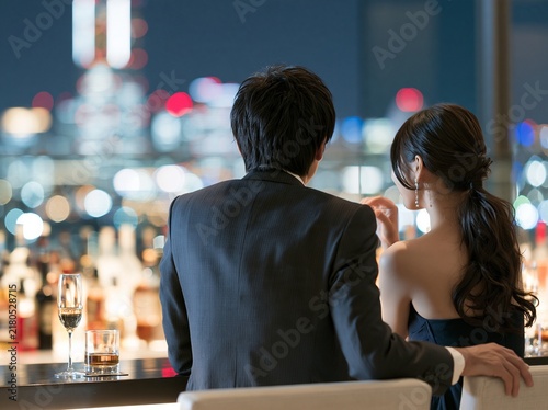 バーカウンターから美しい高層ビルの夜景を望むドレスアップした二人