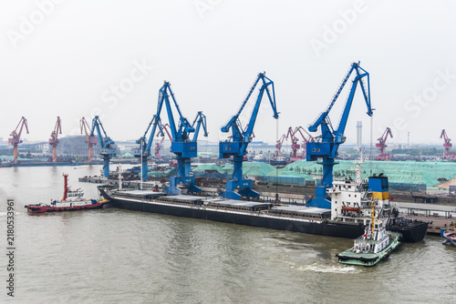 фотографія Large bulk carrier approaching a riverside terminal near Shanghai, China, accompanied by tugboats assisting with the berthing maneuver, illustrating commercial river shipping and port operations