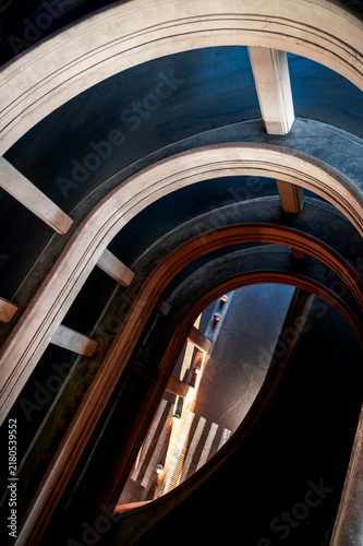A street structure with repeating arches, geometric curves, and dramatic lighting. Vertical color photograph