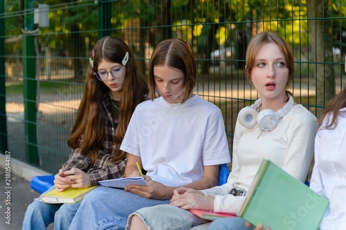 Group of teenage high school girls sit together outdoors with notebooks and school supplies while studying and talking during a break.
