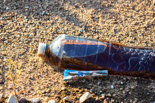 Foto Discarded plastic bottle filled with murky dark liquid resting on a sandy shore
