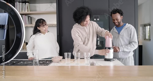 Diverse friends assembling pink blender cup onto white base at kitchen island, camera cue starting