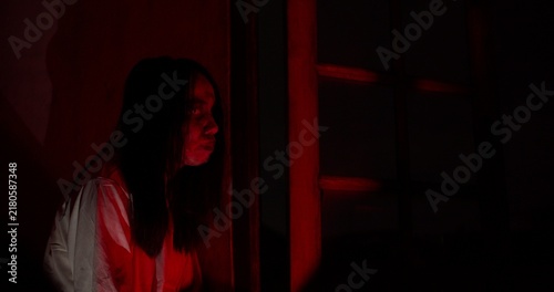 Obraz na plátně A terrifying ghost with a bloody face lurks in a dark, haunted house, illuminated by sinister red light for a horrifying Halloween scene