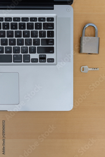 Vertical top view of laptop with padlock and key on wooden desk