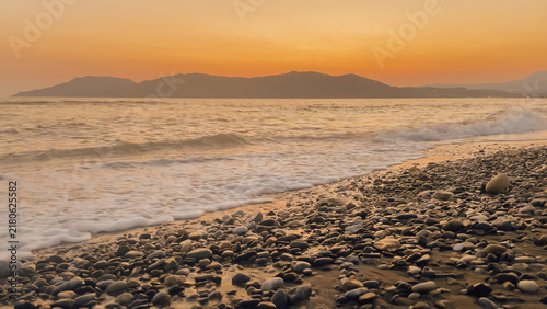 Bild auf Leinwand Scenic view of a rocky beach at sunset with gentle waves lapping against the sho