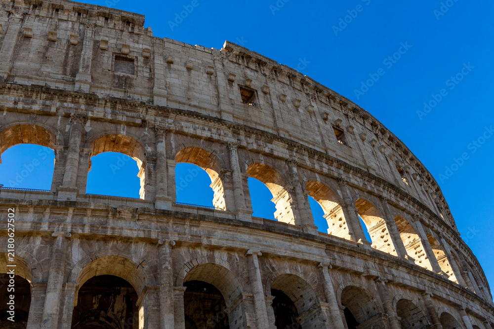 Fototapeta premium Famous Coliseum in Rome. Colosseum, or Coliseum. Part of the wall of an antique stone structure with arches. Italy, Europe. Famous touristic place in the world, Europe. Beautiful blue sky background.