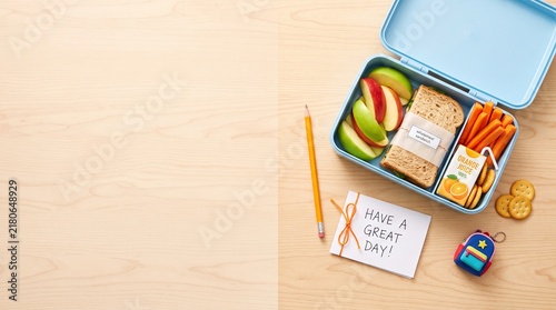 Back to school lunch box flat lay with healthy snacks, sandwich, apple slices, carrot sticks and juice, colorful school essentials on wooden surface with clean white copy space
