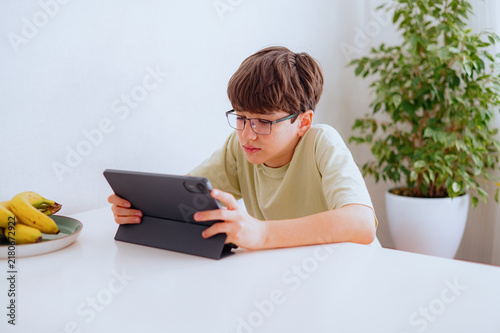 Boy holding tablet, studying or playing, sitting at a white table