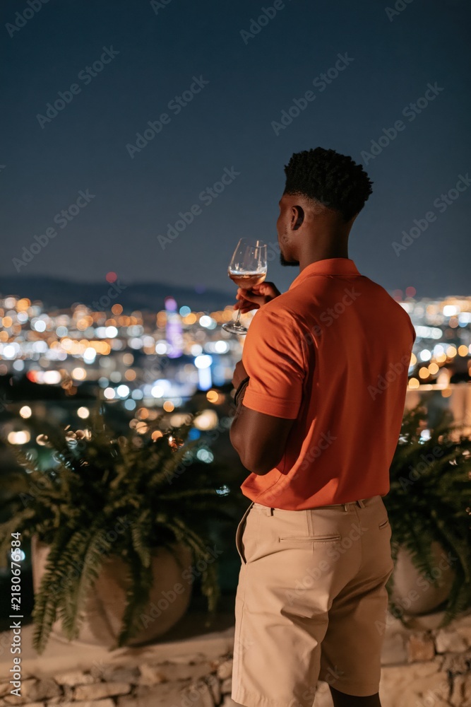 Obraz premium Man on rooftop terrace with wine glass overlooking city skyline at night for lifestyle background and evening relaxation scene