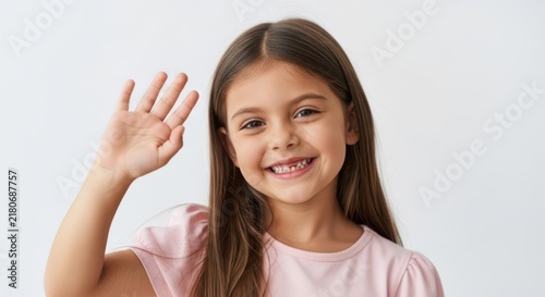 Happy little girl smiling and waving her hand to say hello while looking at the camera in a friendly cheerful mood
