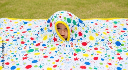 Cute little baby wrapped in a colorful soft hooded towel with bright star and circle patterns playing at home
