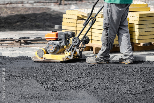 Bild auf Leinwand A person operates a compactor on a black asphalt surface in a construction area