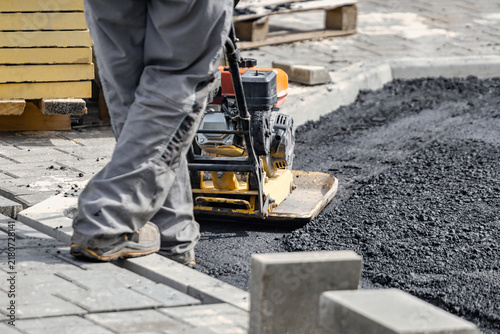 Fotografía A person operates a compactor machine to flatten freshly laid asphalt on a busy street