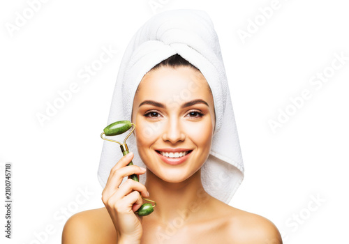 Woman with a towel on her head smiling and using a jade roller for facial massage and skincare.