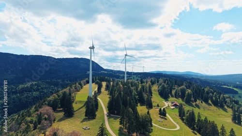 Aerial view of Sainte-Croix wind farm with tall wind turbines set amidst green hills, dense forests, and winding paths in Sainte-Croix, Vaud, Switzerland.