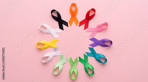 A vibrant collection of colorful awareness ribbons are carefully arranged in a circular formation on a soft pale pink backdrop symbolizing unity and