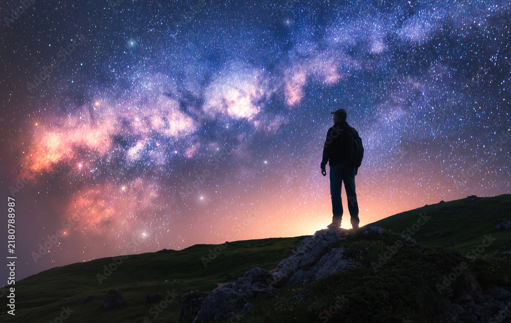 Fototapeta premium Glowing Milky Way and man on mountain peak at starry night. Silhouette of a guy on the hill, sky with bright stars. Galaxy. Space landscape with milky way. Nightscape. Travel background. Concept