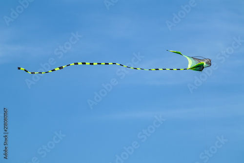 Bild auf Leinwand Close-up of black and green kite toy with long striped tail flying in blue sky