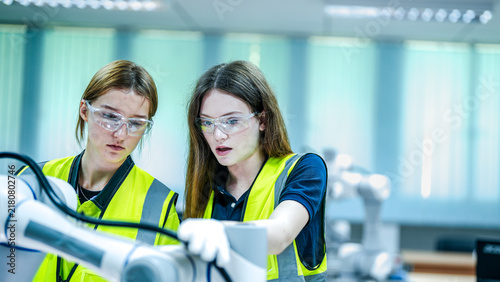 Two female robotics engineers in an R and D lab test an artificial intelligence cobot. They are smiling  inspecting the advanced prototype hardware  sensors  and programming.