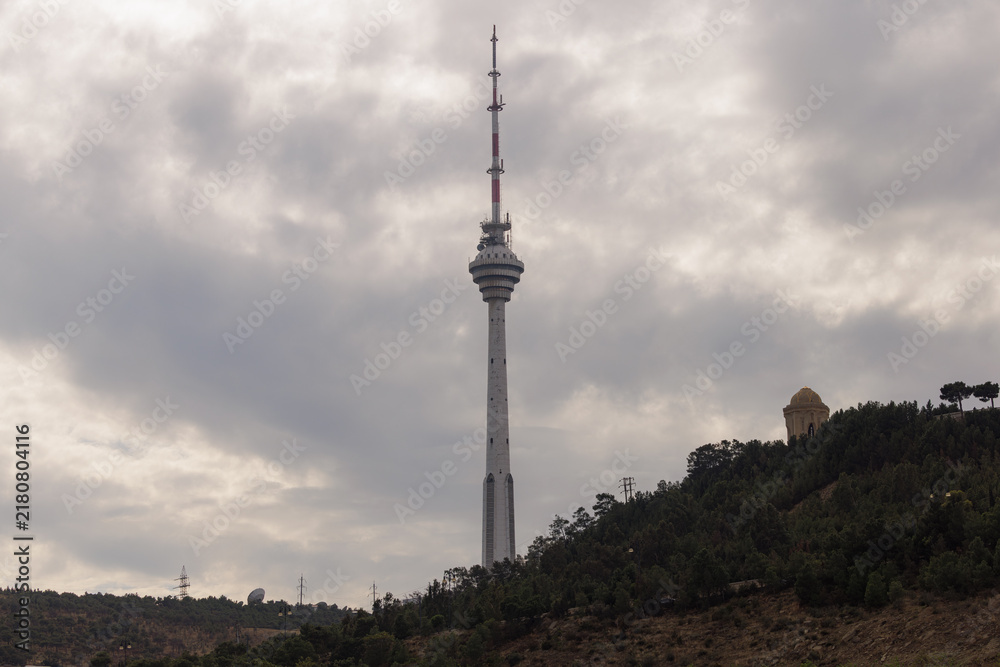 Obraz premium Majestic tower rises above green landscape under a moody sky, showcasing urban engineering wonders