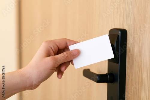 Light-skinned person using a blank white key card to unlock a modern hotel room door, close-up of hand near black electronic lock and warm oak door