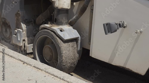 Close up of asphalt milling machine wheel moving along concrete curb during road repair and pavement reconstruction.
