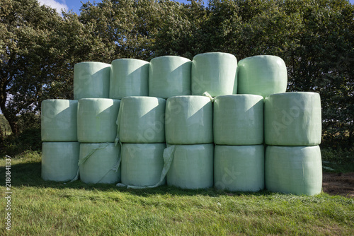 Bales of pre-dried hay are neatly stacked and wrapped in green plastic on a grassy field in the Netherlands
