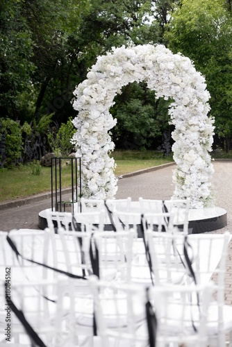 Outdoor wedding ceremony venue with white flower arch and chiavari chairs
