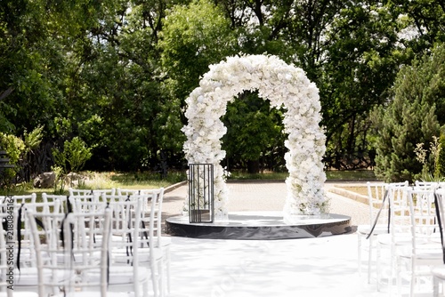 Outdoor wedding ceremony venue with white flower arch and chiavari chairs