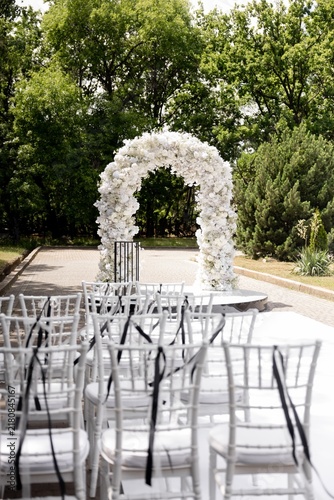 Outdoor wedding ceremony venue with white flower arch and chiavari chairs