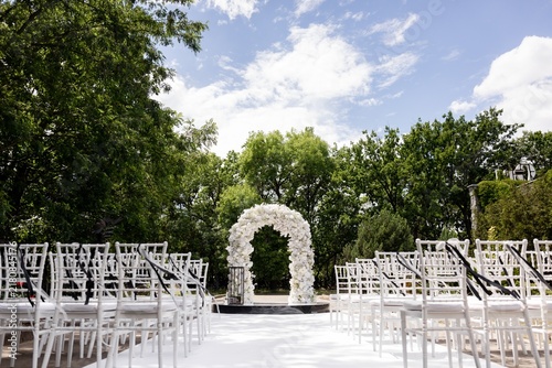 Outdoor wedding ceremony venue with white flower arch and chiavari chairs