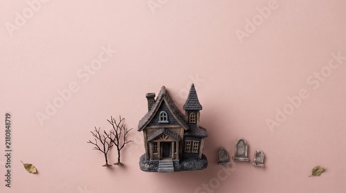 Miniature haunted house model with small bare trees and tombstones on a light pink background for halloween decoration