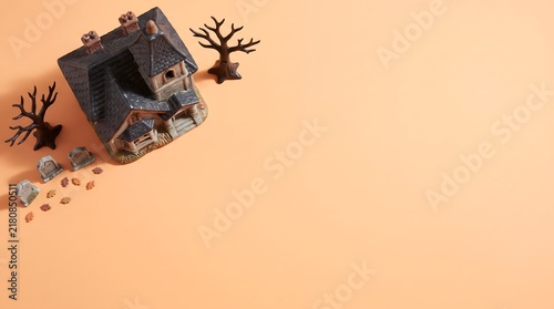 Miniature spooky haunted house with dead trees and small tombstones on a light orange background for halloween celebration