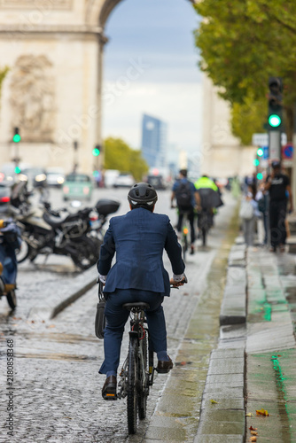 Businessman in a suit rides a bicycle toward the Arc de Triomphe on a wet Paris street, symbolizing sustainable urban transportation and commuting