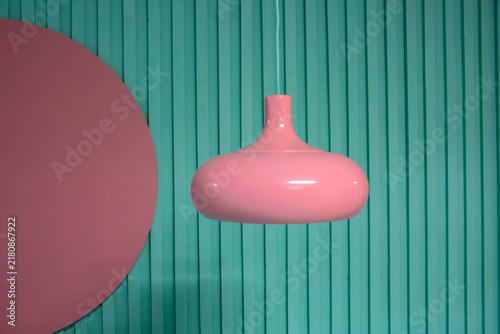 Pink pendant lamp hanging against a teal striped background with a pink circle shape, high quality photo
