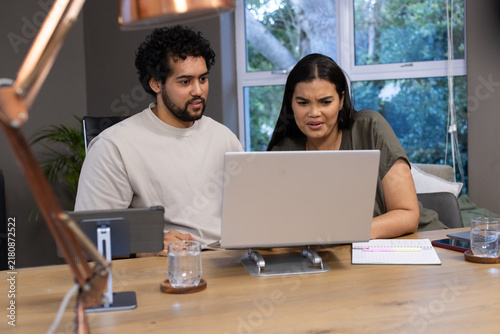 African American couple leaning forward and frowning at laptop on metal stand at home