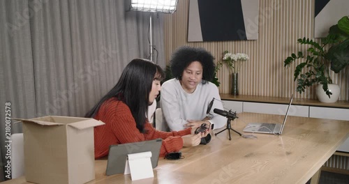 African American friends reaching into box, unboxing wearable device, reviewing via laptop mic