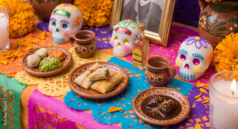 Fototapeta premium Festive Dia de los Muertos ofrenda table decorated with brightly decorated painted skulls clay dishes pan de muerto and yellow marigold petals