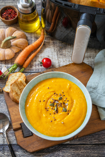 Homemade pumpkin vegetarian soup in kitchen gadget modern air fryer on wooden background.
