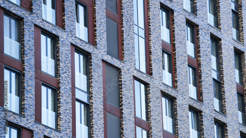 Modern residential building facade with geometric brickwork, large windows and glass balcony elements, illustrating contemporary urban housing, real estate development and modern architecture