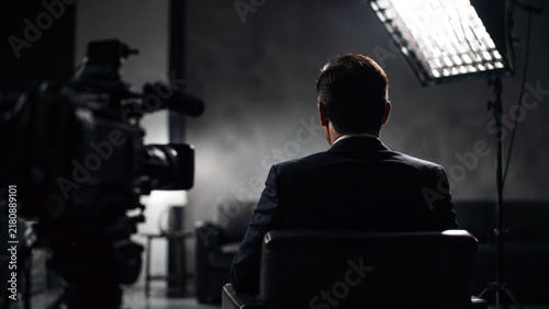 Businessman sitting with his back to the camera during a filmed studio interview with professional video and lighting equipment